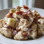Close-up of creamy honey mustard chicken salad chunks topped with crispy bacon bits and green apple pieces.
