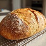 A freshly baked loaf of Italian bread with a golden, crackly crust dusted with flour, cooling on a wire rack.