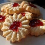 Close-up of star-shaped Italian butter cookies topped with bright red jam on a white plate.