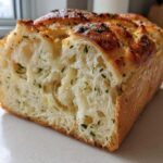 Close-up of a freshly baked loaf of Italian herb and cheese bread, showing the soft, airy interior texture.