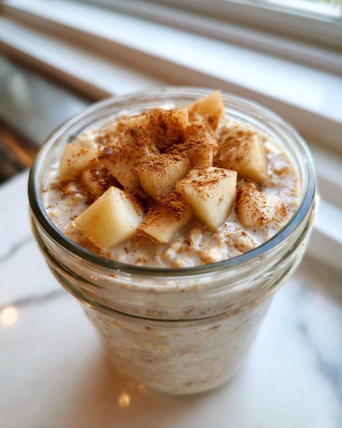 Close-up of apple cinnamon overnight oats in a glass jar, topped with diced apples and cinnamon.