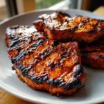 Close-up of several perfectly grilled and glazed pork steak recipe cuts piled on a plate.