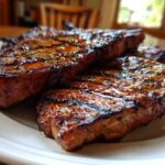 Close-up of three juicy, glazed pork steak recipe cuts with prominent grill marks on a white plate.