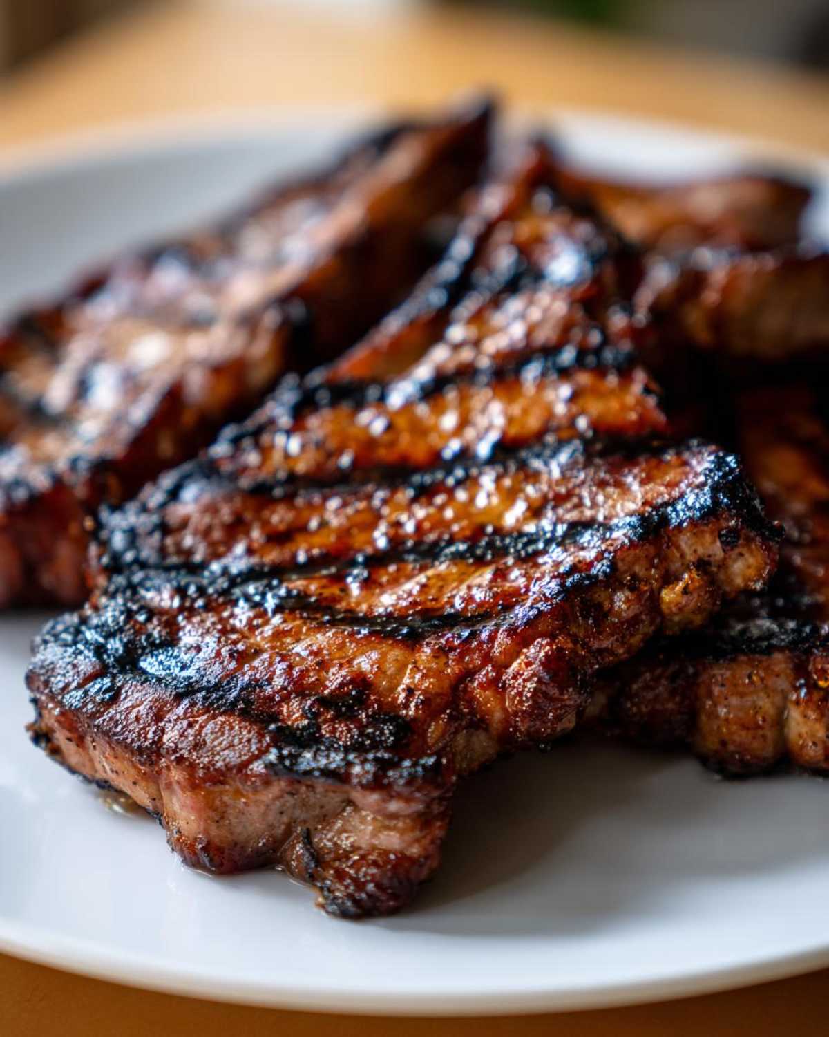 Close-up of several juicy grilled pork steak cuts showing dark, caramelized grill marks on a white plate.