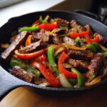 Close-up of sizzling steak fajitas with colorful peppers and onions in a cast iron skillet.