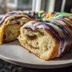 A slice cut from a homemade king cake showing the soft, layered interior and Mardi Gras colored icing.