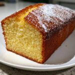 A golden brown loaf of lemon olive oil cake, drizzled with white glaze and dusted with powdered sugar.