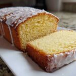 Close-up of a sliced lemon olive oil cake loaf drizzled with white glaze on a white platter.