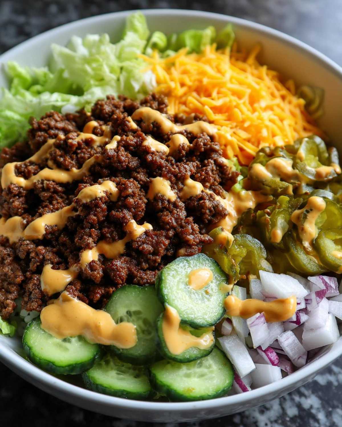 Close-up of a delicious cheeseburger bowl featuring seasoned ground beef, shredded cheese, lettuce, pickles, and sauce.