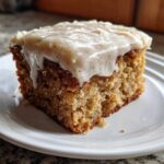 Close-up of a moist slice of applesauce cake topped with thick, spiced cream cheese frosting.