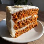 A tall slice of moist carrot cake recipe with three layers and thick cream cheese frosting.