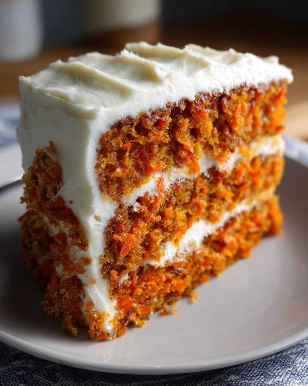 A close-up of a thick slice of moist carrot cake recipe layered with rich cream cheese frosting.
