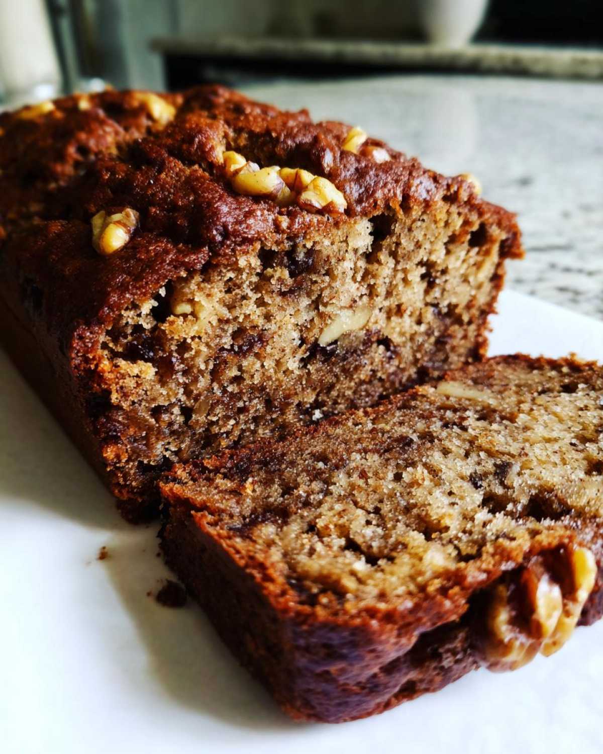 Close-up of moist date nut bread loaf with a slice cut, topped with visible walnuts.