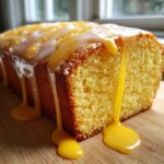 Close-up of a moist lemon pound cake loaf dripping with bright yellow and white glaze on a wooden board.