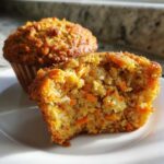 Close-up of a morning glory muffin cut in half showing moist texture, shredded carrots, and coconut.