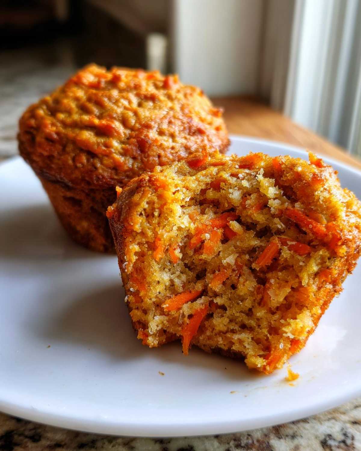 Close-up of a morning glory muffin broken in half showing the moist interior packed with shredded carrots.