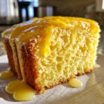 Close-up of a moist slice of bright yellow lemon pound cake generously topped with a thick, dripping lemon glaze.