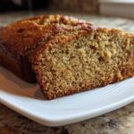 A close-up of a loaf of sugar free banana bread with one thick slice cut, showing the moist, textured crumb.