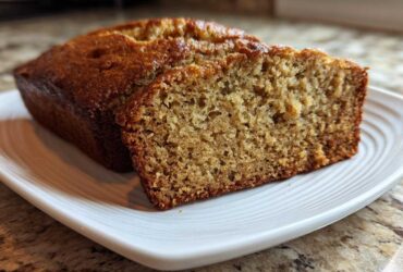 A close-up of a loaf of sugar free banana bread with one thick slice cut, showing the moist, textured crumb.
