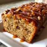 Close-up of moist sweet alabama pecan bread loaf topped with pecans and dripping with caramel sauce.