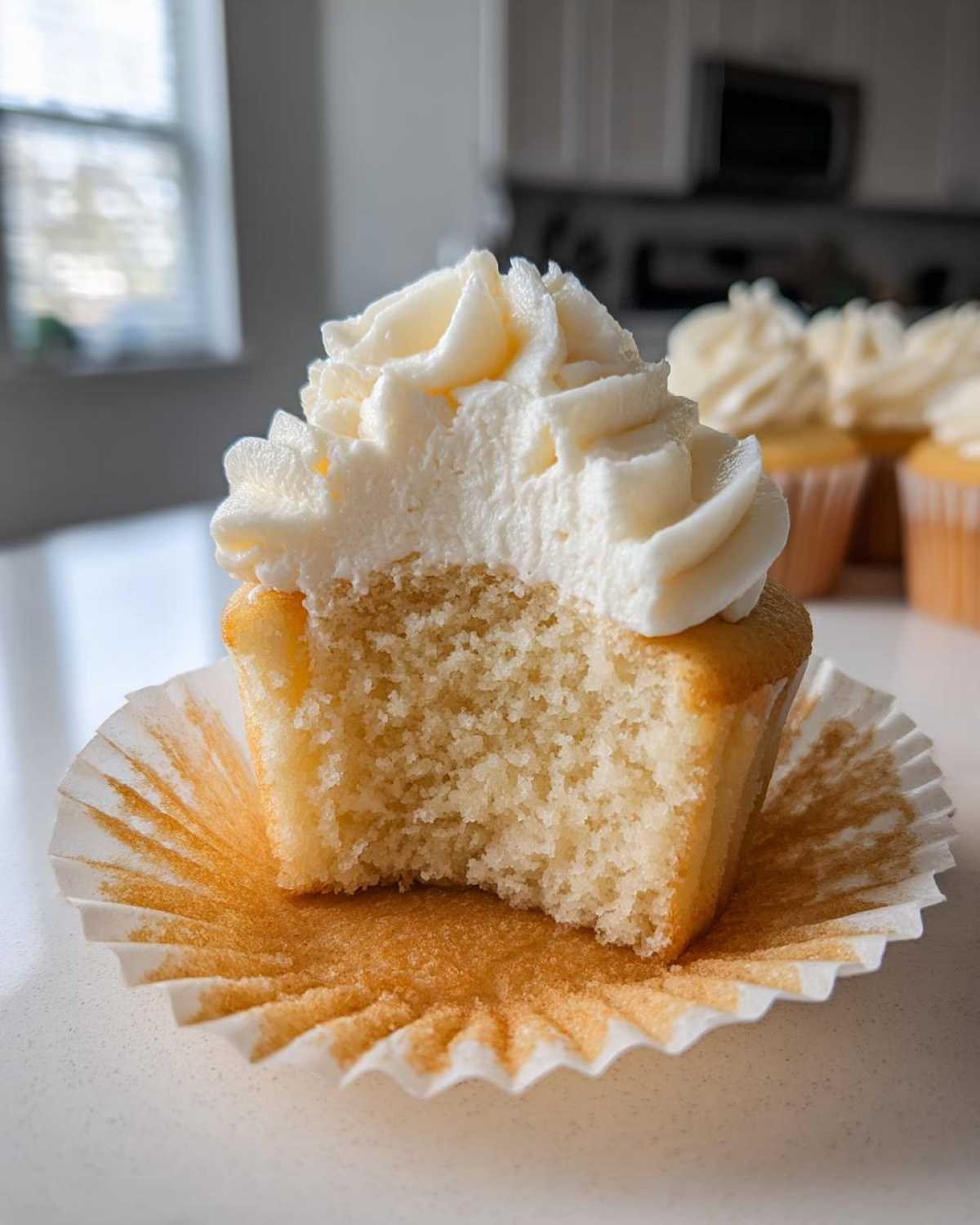 Close-up of a moist vanilla cupcakes with a bite taken out, showing the fluffy interior and white frosting.