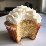 Close-up of a moist vanilla cupcakes with fluffy white frosting, showing the soft interior texture after a bite was taken.