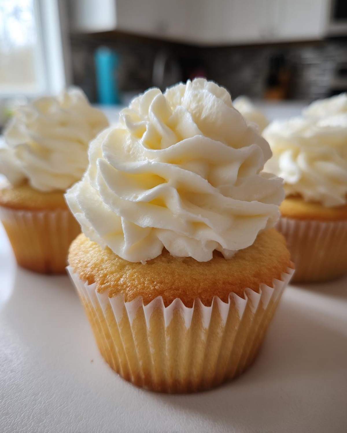 Close-up of a moist vanilla cupcakes topped with a tall swirl of white vanilla buttercream frosting.