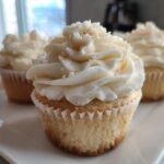 Close-up of a moist vanilla cupcake topped with swirled white frosting and sprinkles.