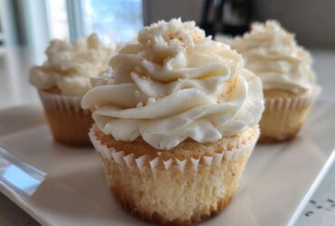 Close-up of a moist vanilla cupcake topped with swirled white frosting and sprinkles.