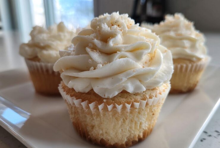 Close-up of a moist vanilla cupcake topped with swirled white frosting and sprinkles.