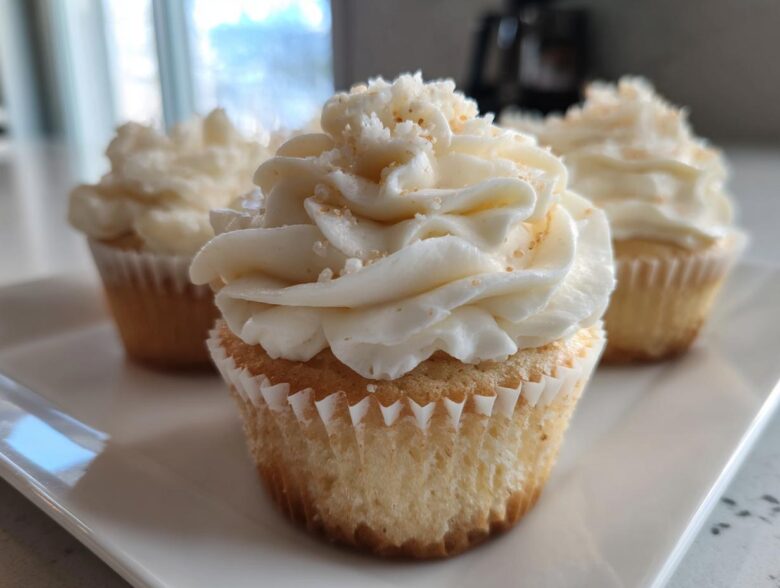 Close-up of a moist vanilla cupcake topped with swirled white frosting and sprinkles.