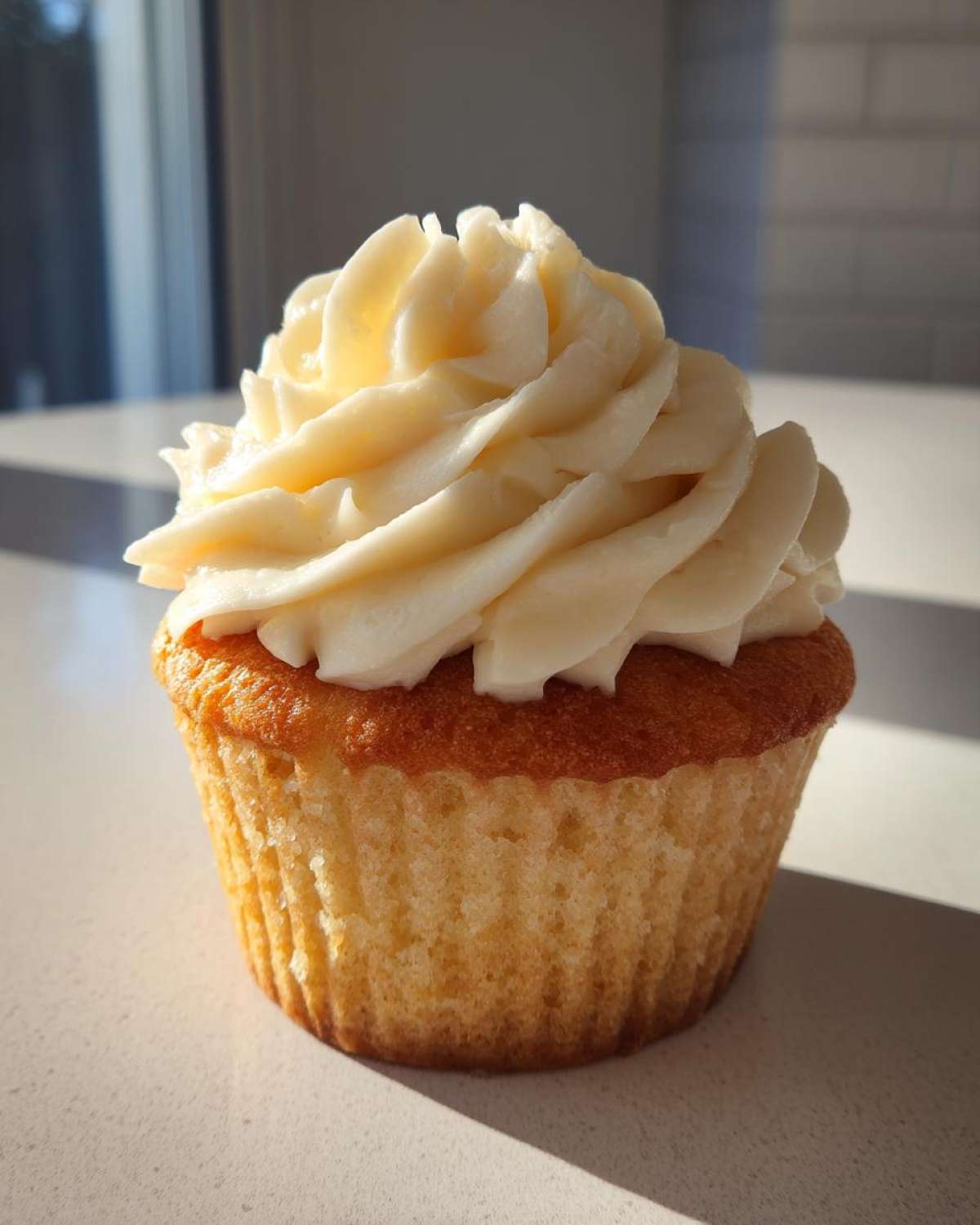 Close-up of a single, perfectly baked vanilla cupcake topped with a swirl of creamy white vanilla frosting.
