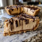 A thick slice of creamy no-bake peanut butter pie with a graham cracker crust and rich chocolate drizzle.