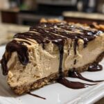 A thick slice of creamy no-bake peanut butter pie on a white plate, topped with rich chocolate syrup drizzle.