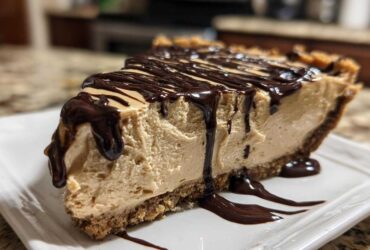 A thick slice of creamy no-bake peanut butter pie on a white plate, topped with rich chocolate syrup drizzle.