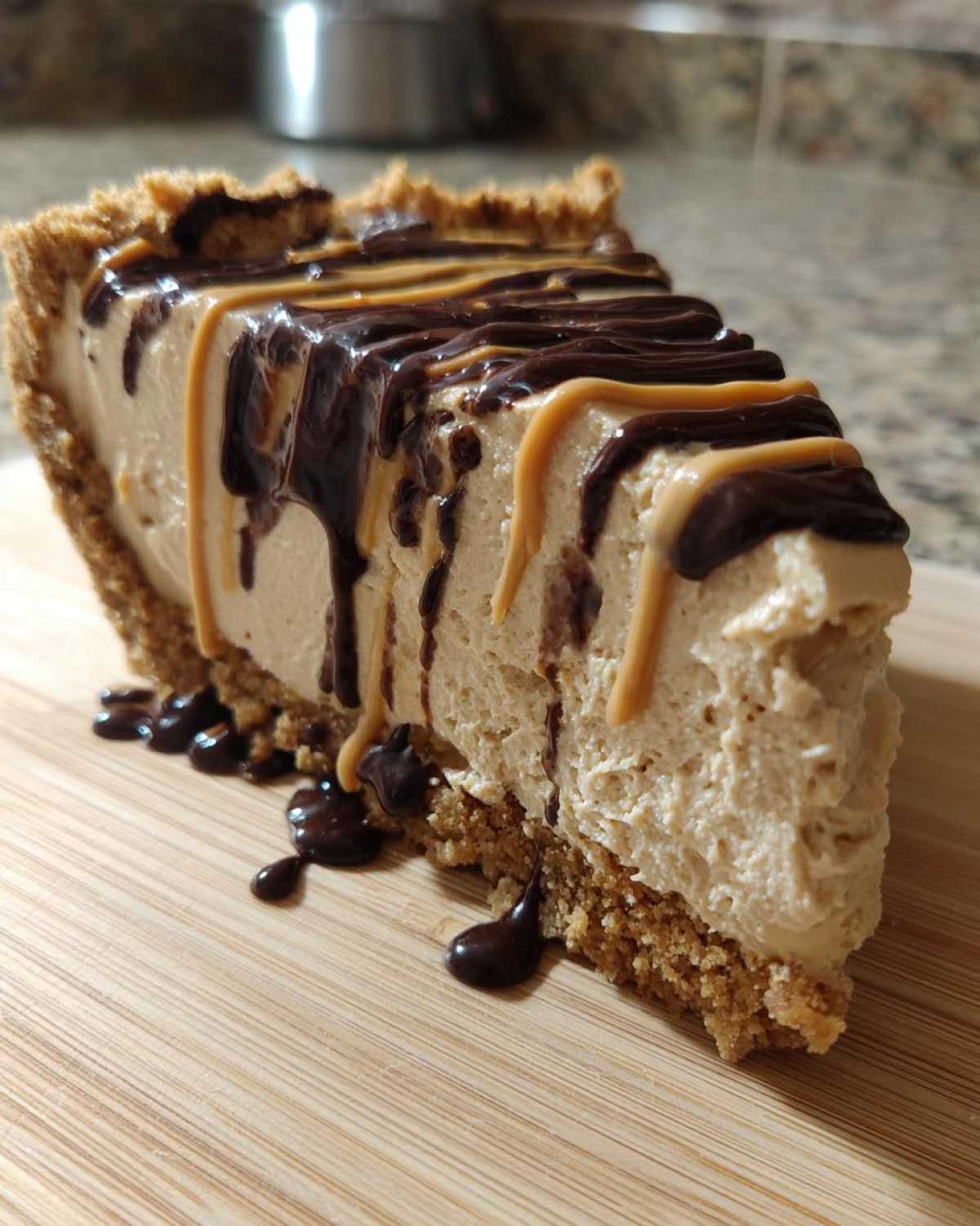A decadent slice of no-bake peanut butter pie with a graham cracker crust, drizzled with chocolate and peanut butter sauce.