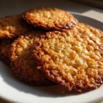 Close-up of several golden brown, lacy oatmeal lace cookies stacked on a white plate.