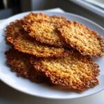 A stack of golden brown, delicate oatmeal lace cookies showing their intricate, lacy edges on a white plate.