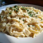 A close-up of fettuccine pasta coated in rich olive garden alfredo sauce, topped with parmesan and parsley.