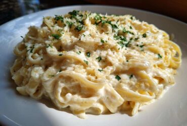 A close-up of fettuccine pasta coated in rich olive garden alfredo sauce, topped with parmesan and parsley.