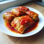 A close-up of four hearty cabbage rolls smothered in rich tomato sauce, served on a white plate.