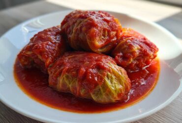 Four savory cabbage rolls smothered in a vibrant red tomato sauce served on a white plate.