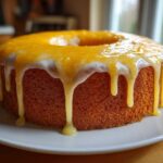 A golden brown orange juice cake with thick white and bright orange glaze dripping down the sides.
