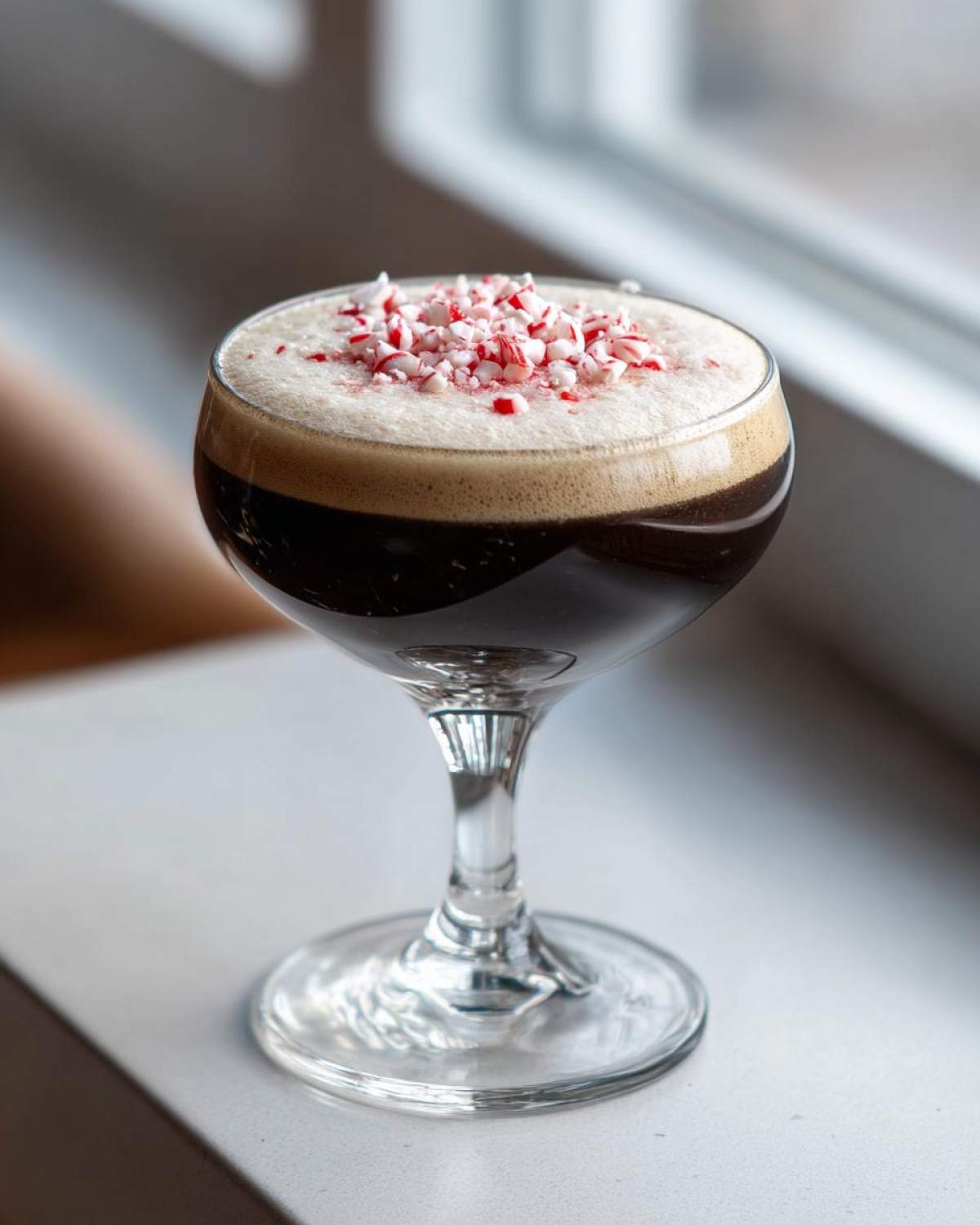 A festive peppermint espresso martini topped with crushed candy canes, served in a coupe glass.