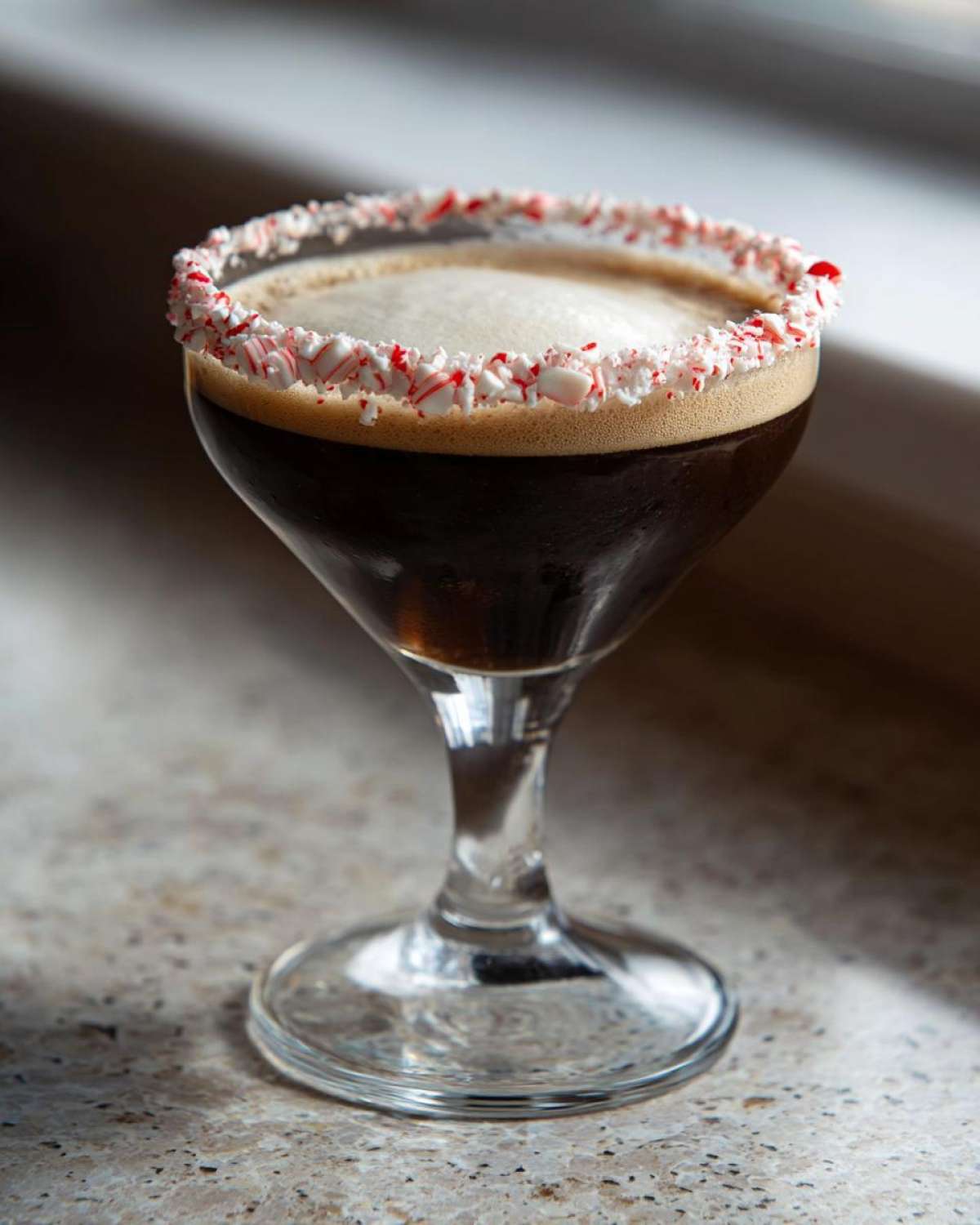 A dark peppermint espresso martini in a coupe glass with a crushed candy cane rim.