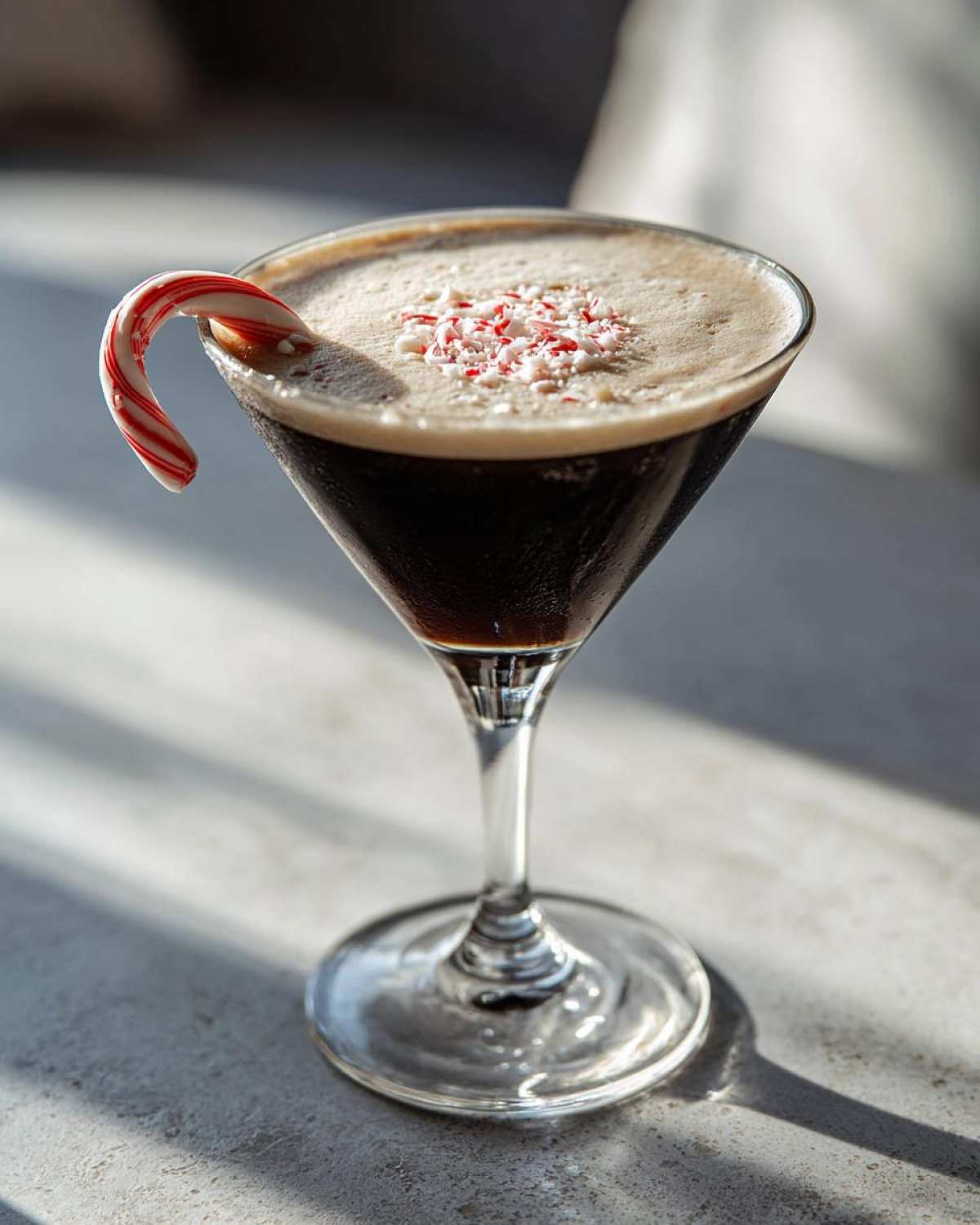 A festive peppermint espresso martini in a coupe glass, garnished with a candy cane and crushed peppermint.