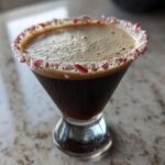 A dark peppermint espresso martini in a martini glass with a crushed candy cane rim.