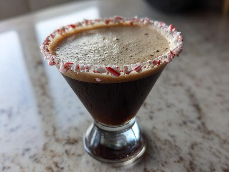 A dark peppermint espresso martini in a martini glass with a crushed candy cane rim.