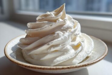 A beautiful, tall swirl of fluffy white cream cheese frosting piped onto a small, rustic saucer.
