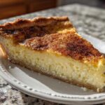 A thick slice of creamy baked egg custard pie with a golden, cinnamon-sugar dusted top.